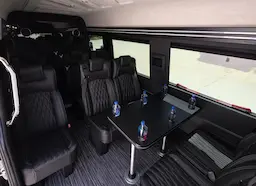 Inside executive sprinter with front and rear facing leather chairs, table, tv and premium waters